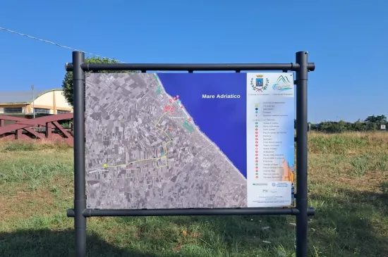Cartello turistico mostra mappa costiera con mare blu e campagna verde.